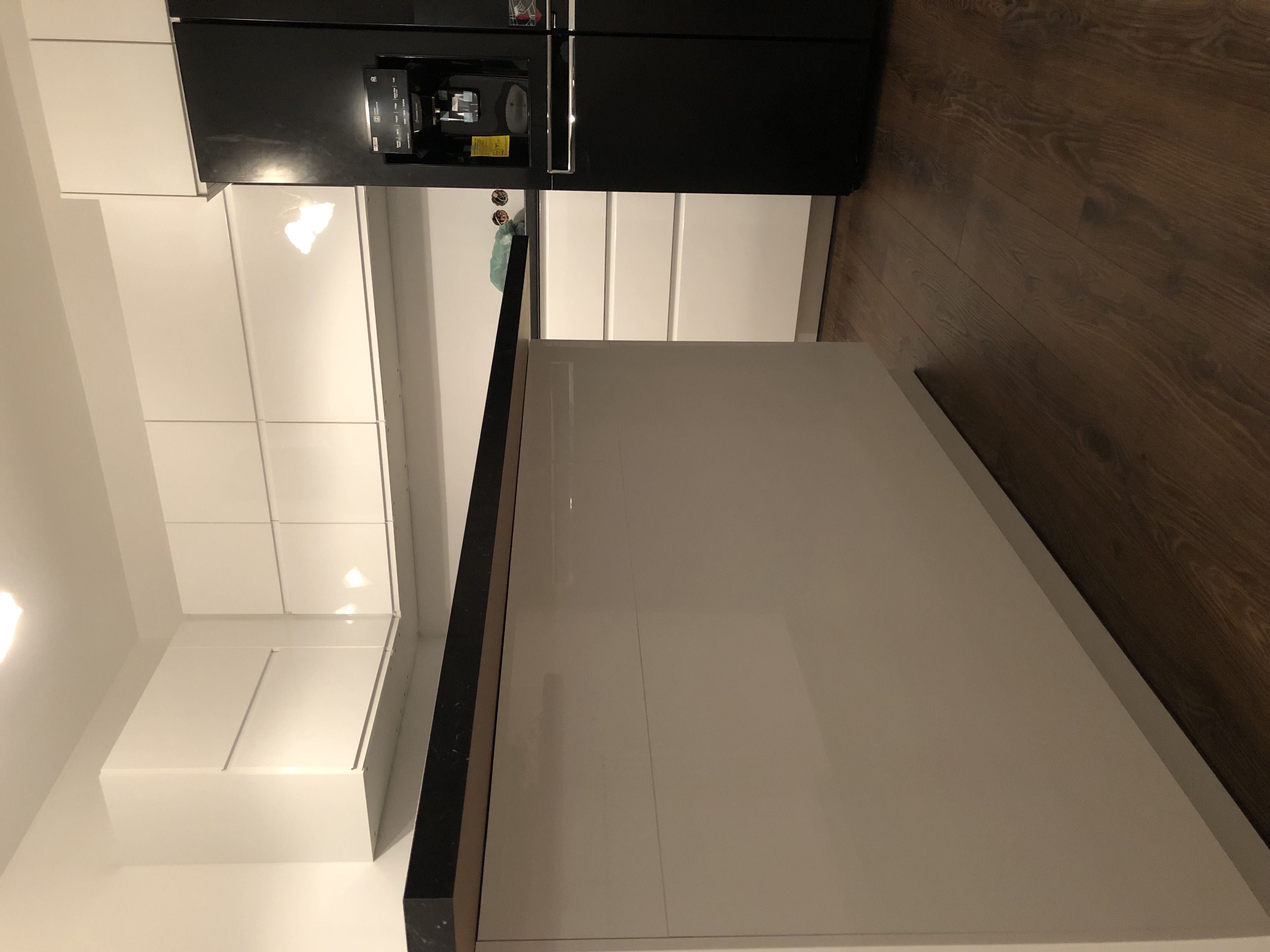 Nowoczesna kuchnia z białą zabudową, czarnym blatem i ciemną drewnianą podłogą, oświetlona ciepłym światłem.