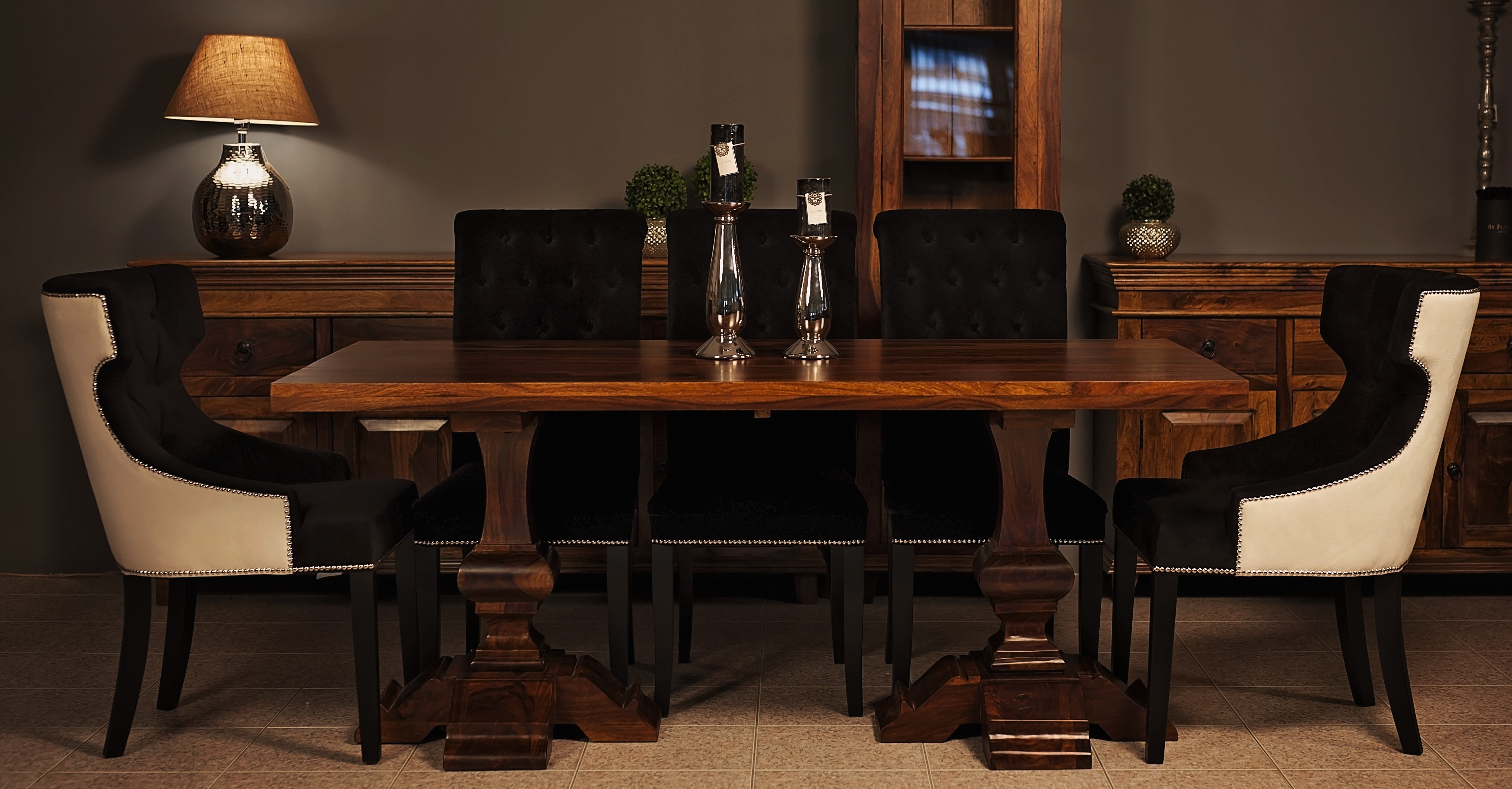 Jadalnia z drewnianym stołem na masywnych nogach, czarnymi krzesłami z tapicerowanymi oparciami i kremowymi bokami, oraz komodami w tle