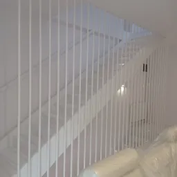 Nowoczesne, białe schody z minimalistyczną balustradą z pionowych prętów, częściowo zasłonięte folią ochronną, sugerujące prace wykończeniowe.