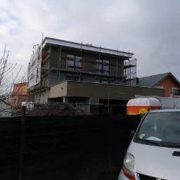 Budowa domu murowanego w Nowym Mieście nad Wartą w trakcie ocieplania elewacji, widoczne rusztowania i tymczasowa toaleta.