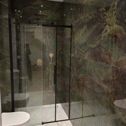 Daniel Szymańczak - Nowoczesna łazienka z kabiną prysznicową typu walk-in z czarnymi ramami, armaturą w kolorze szczotkowanego złota i płytkami imitującymi zielony marmur na ścianach i podłodze, widok na toaletę.