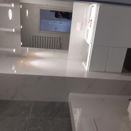 Daniel Szymańczak - Nowoczesna łazienka z białymi marmurkowymi płytkami, szarą podłogą, podświetlanym lustrem i białymi meblami łazienkowymi.