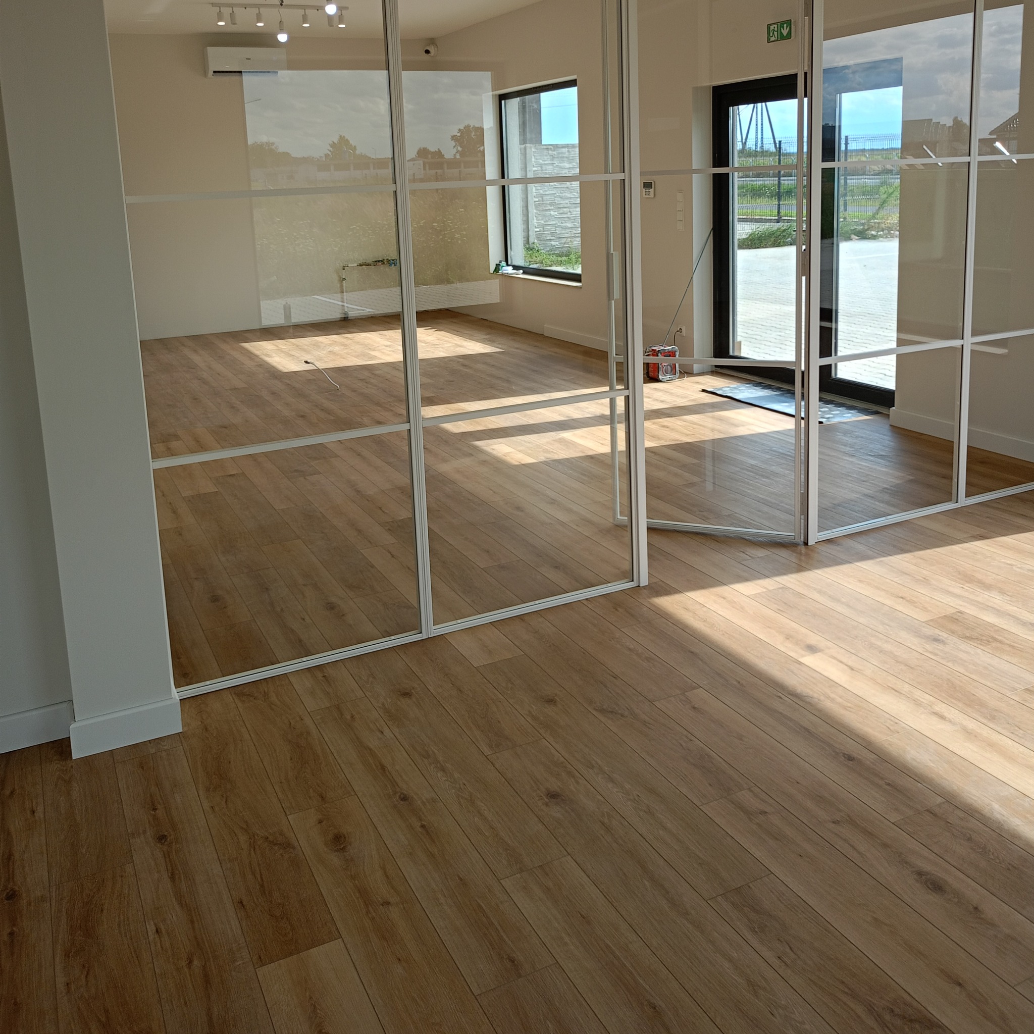 Jasne panele podłogowe ułożone w nowym pomieszczeniu z przeszklonymi ścianami działowymi i widokiem na zewnątrz.