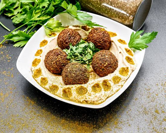 Porcja falafela na hummusie, udekorowana świeżą pietruszką i posypana przyprawami, podana na białym talerzu z przyprawami w tle.