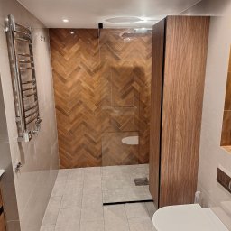 NakoS Przemysław Zieliński - Nowoczesna łazienka z kabiną prysznicową typu walk-in, wykończona płytkami w jodełkę. Widoczny grzejnik drabinkowy i podwieszana toaleta. Minimalistyczny design.