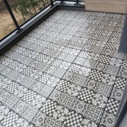 Wzorzyste, szare i białe płytki podłogowe ułożone na balkonie z czarną balustradą, widok z góry pod kątem.