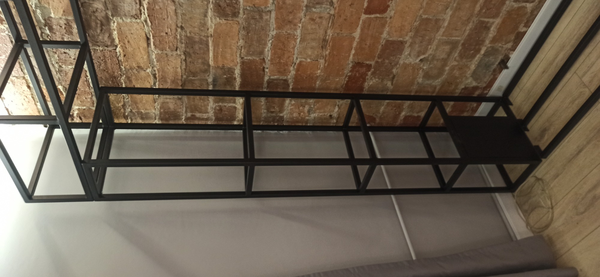 Metalowa konstrukcja regału spawanego z profili kwadratowych, widoczna na tle ceglanego sufitu i jasnej ściany.