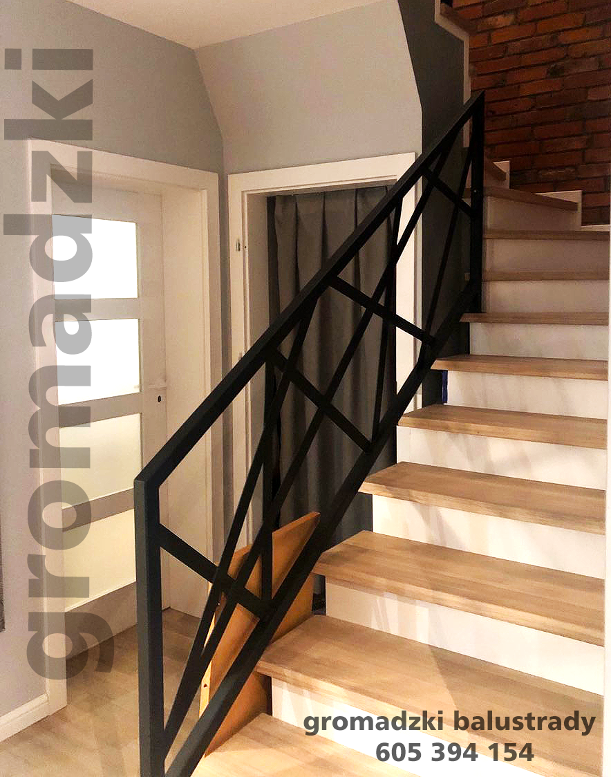 Schody z drewnianymi stopniami i nowoczesną, czarną, metalową balustradą o geometrycznym wzorze, widok z dołu, ściana z cegły w tle.