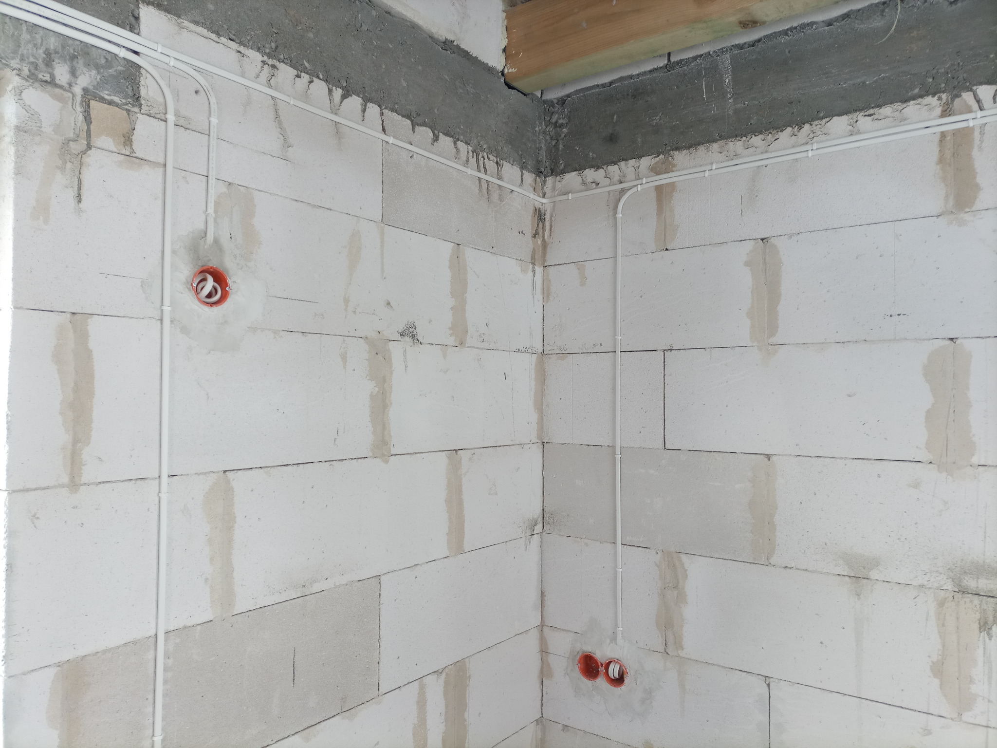 Świeżo położona instalacja elektryczna w białych rurkach, z widocznymi puszkami pod gniazdka na ścianie z betonu komórkowego, w surowym stanie.