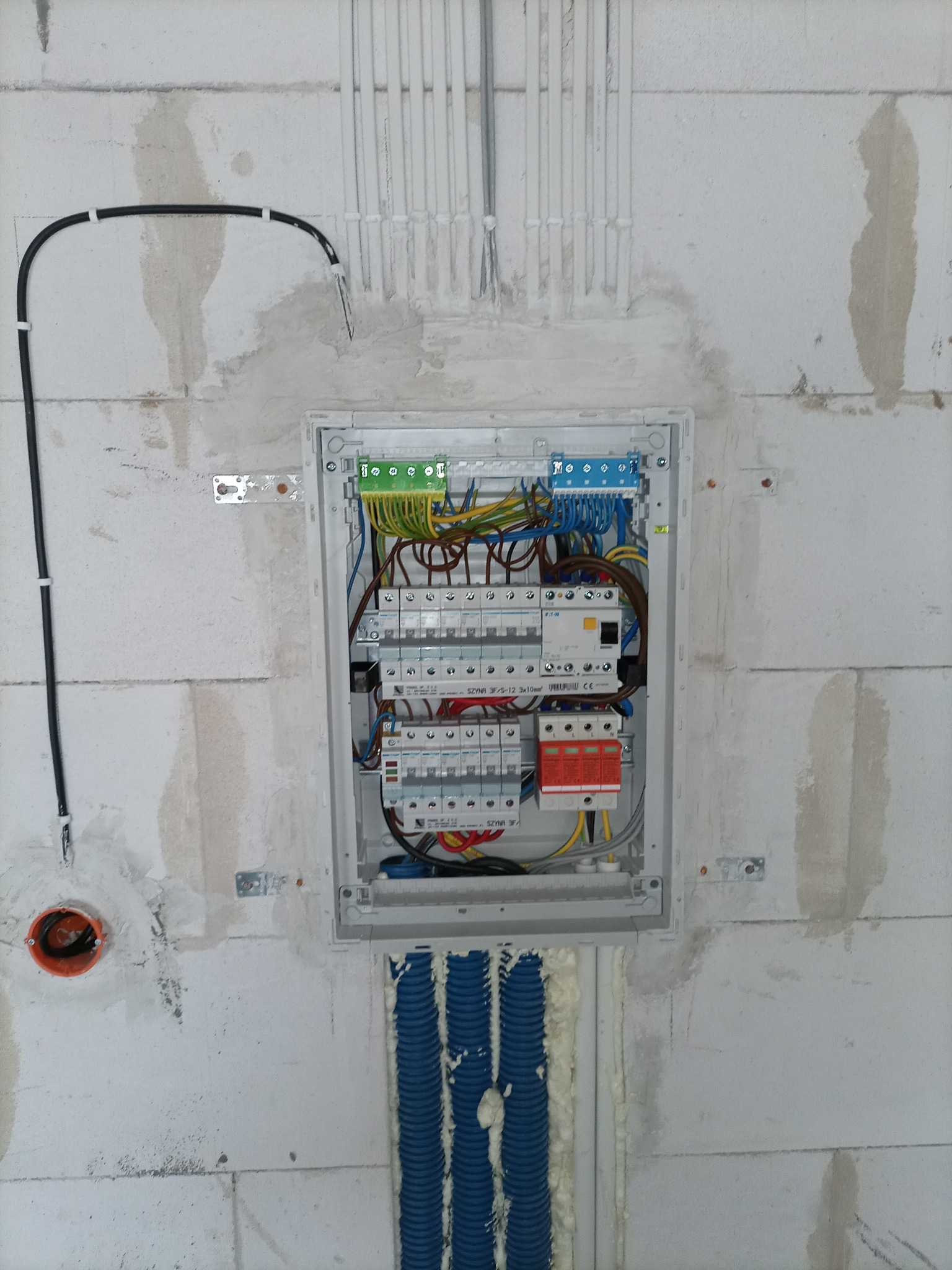 Rozdzielnica elektryczna wmurowana w ścianę z betonu komórkowego, widoczne kable, przewody i zabezpieczenia, instalacja w trakcie montażu.