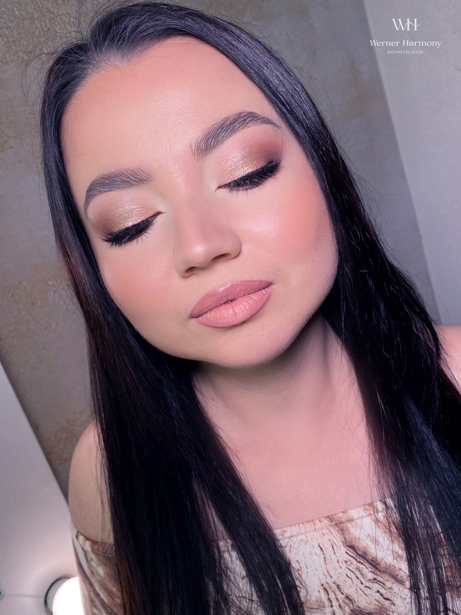 Portret kobiety z zamkniętymi oczami, prezentującej delikatny, połyskujący cień na powiekach i subtelny róż na policzkach, z idealnie wyregulowanymi brwiami i błyszczącymi, nude ustami.