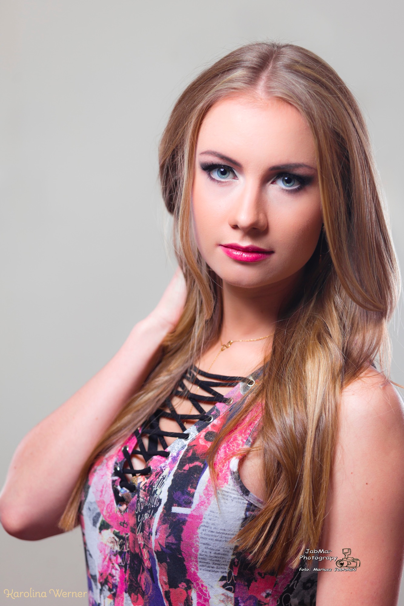 Portret kobiety z profesjonalnym smoky eye i różowymi ustami, wykonany w Krakowie. Modelka w bluzce z czarnym sznurowaniem i kolorowym wzorem, delikatnie dotyka szyi.
