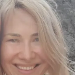 Uśmiechnięta blond kobieta z lekkim makijażem na tle jasnej skały.