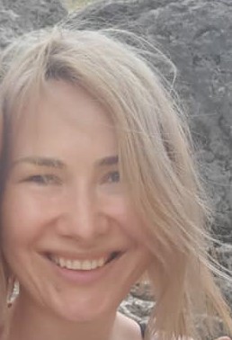 Uśmiechnięta blond kobieta z lekkim makijażem na tle jasnej skały.