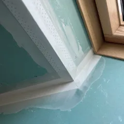 Połączenie płyty karton gips z oknem dachowym w trakcie prac wykończeniowych, widoczna taśma wzmacniająca i wstępne warstwy szpachli.