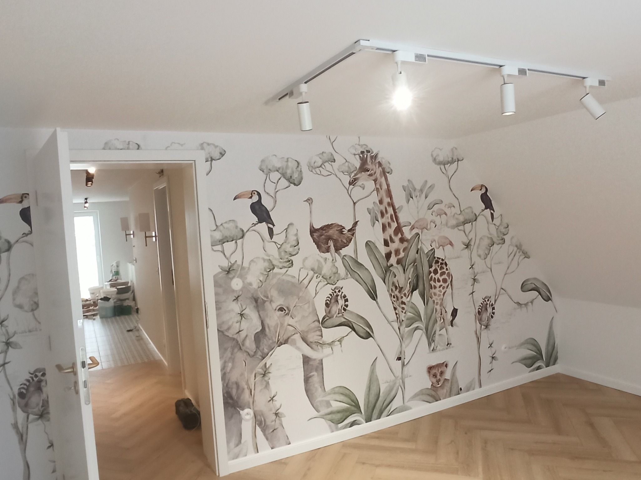 Pokój dziecięcy z fototapetą w motywy zwierząt: słoń, żyrafa, tukany, lemury, oświetlenie szynowe, parkiet w jodełkę.