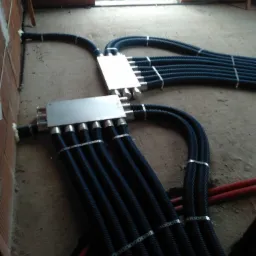 Rozdzielacz kanałów wentylacyjnych z podłączonymi rurami karbowanymi na surowym betonowym podłożu w trakcie montażu instalacji w budynku w stanie surowym.