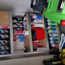 Półka regałowa z preparatami i akcesoriami do czyszczenia, w tle widoczna myjka ciśnieniowa i odkurzacz piorący.