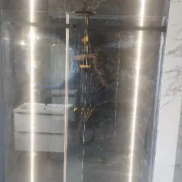 Szklana kabina prysznicowa z deszczownicą w łazience wykończonej marmurem. Widoczne oświetlenie LED i umywalka z szafką.