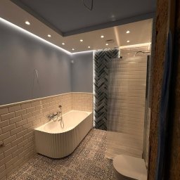 Krzoch-Bud - Nowoczesna łazienka z wanną, toaletą i kabiną prysznicową. Uwagę zwracają dekoracyjne płytki na podłodze i ścianie, oraz oświetlenie LED pod sufitem.