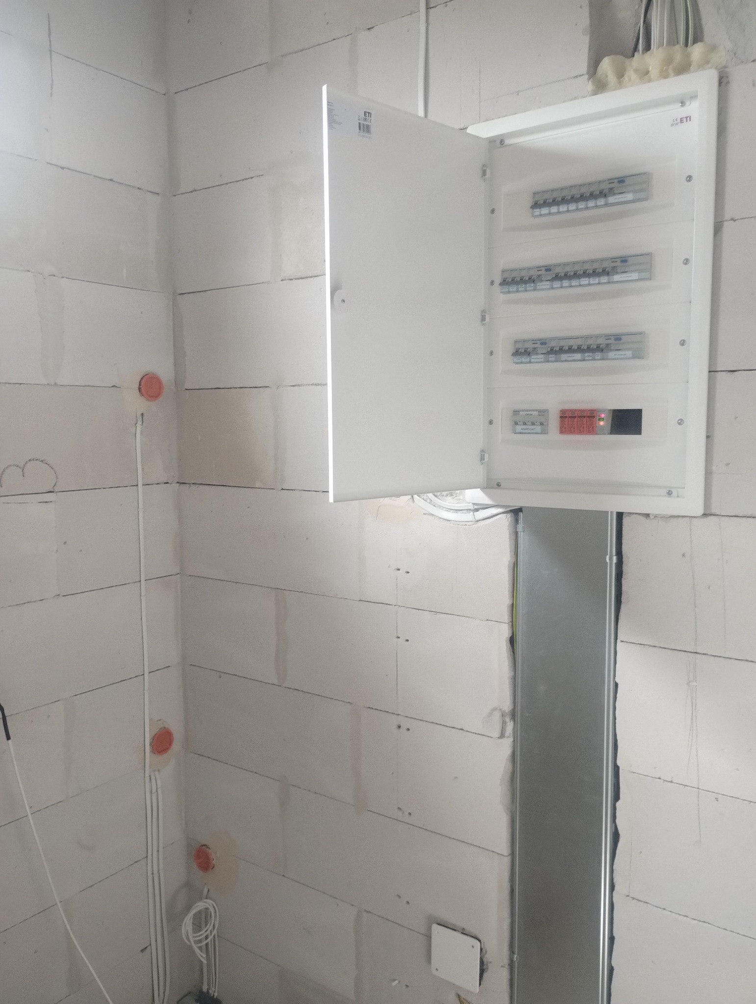 Otwarta skrzynka elektryczna ETI na ścianie z betonu komórkowego. Widoczne zabezpieczenia i okablowanie. Nowa instalacja w surowym wnętrzu.