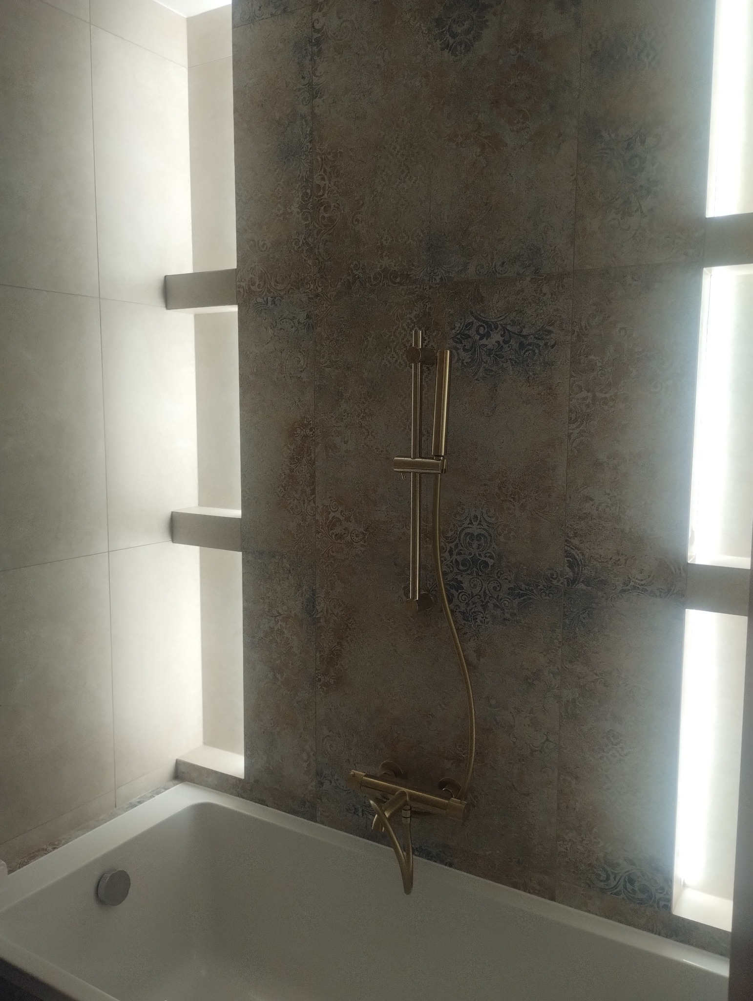 Wykończona łazienka z wanną, złotą armaturą i dekoracyjną ścianą z podświetlanymi niszami. Nowoczesny design z dbałością o detale.