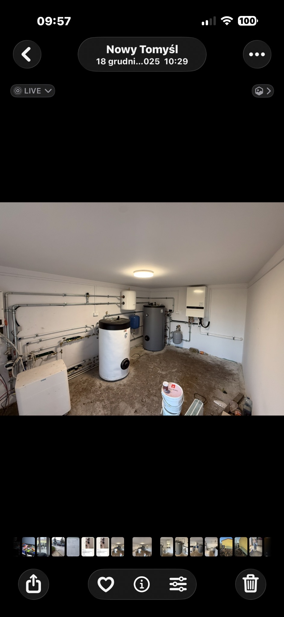 Kotłownia po instalacji: biały i szary zbiornik, piec gazowy na ścianie, rury rozprowadzone wzdłuż ścian. Widok na surową podłogę i pozostałości po pracach.