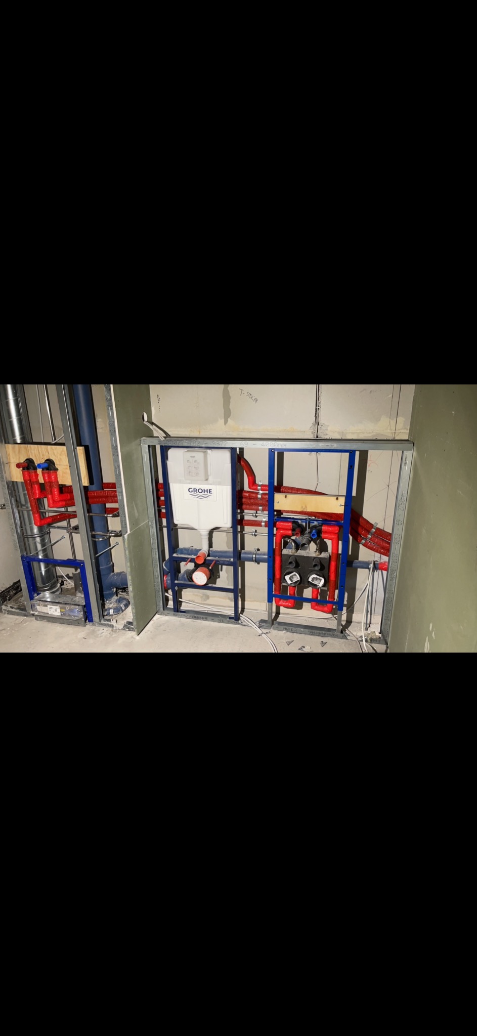 Instalacja podtynkowa WC z widocznymi rurami w izolacji termicznej, zamontowana na stelażu z profili stalowych. Widoczny zbiornik Grohe i fragment ściany z płyt gipsowych.