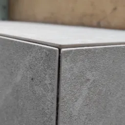 Szczegółowe ujęcie narożnika wykończonego szarą, matową płytką ceramiczną z widoczną fugą, na tle drewnianej konstrukcji i izolacji.