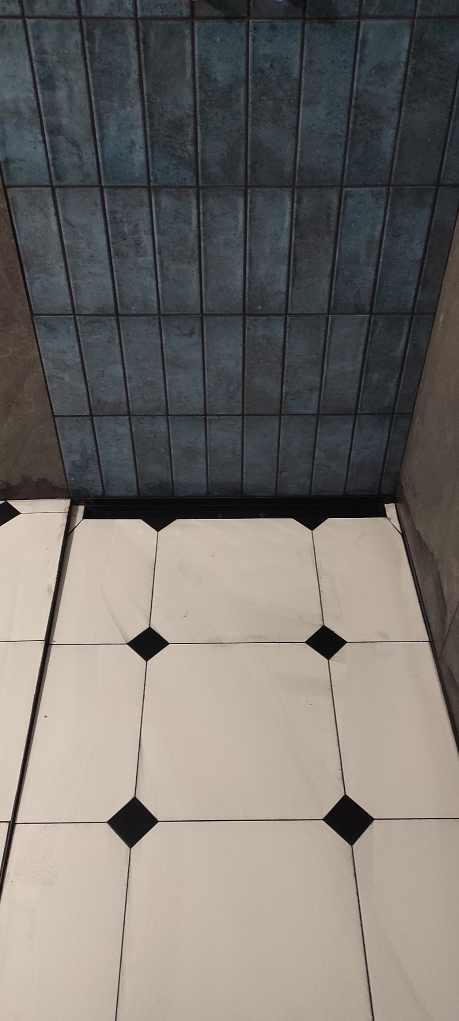 Wykończona łazienka: biało-czarna podłoga z kwadratami i niebieskie, pionowe płytki na ścianie. Widok z góry, ukazujący detale fug i fakturę płytek.