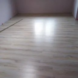 Ułożona podłoga z paneli laminowanych w pustym pokoju z różowymi ścianami, widoczne listwy przypodłogowe i małe czerwone kliny dystansowe przy ścianach.