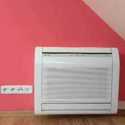 Biały klimatyzator Fuji Electric zamontowany na różowej ścianie w pokoju, widoczny gładki parkiet i fragment ciemnego mebla, obok gniazdko elektryczne z trzema wejściami.