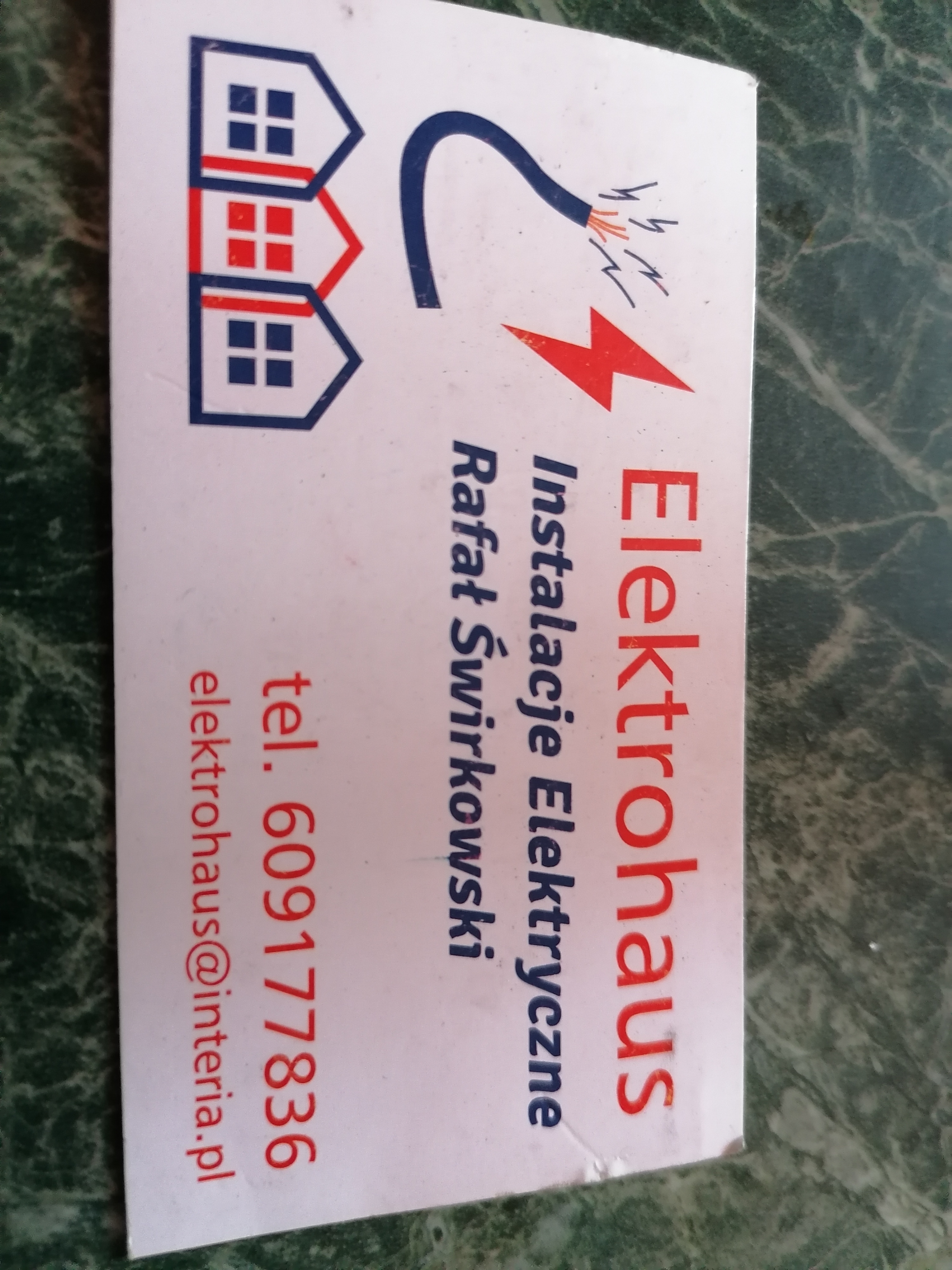 Wizytówka firmy Elektrohaus Rafała Świrkowskiego z numerem telefonu i adresem e-mail, prezentująca logo z domkami i symbolem elektrycznym.
