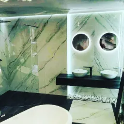 Luksusowa łazienka z zielonymi marmurowymi płytami, podświetlanymi okrągłymi lustrami, dwiema umywalkami nablatowymi i wanną wolnostojącą, wykończona białymi kamykami dekoracyjnymi.