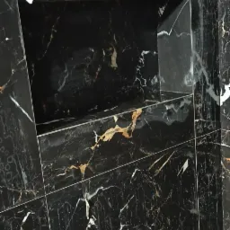 Ściana wyłożona czarnymi płytkami imitującymi marmur z wnęką, widoczne białe i złote żyłki na płytkach.