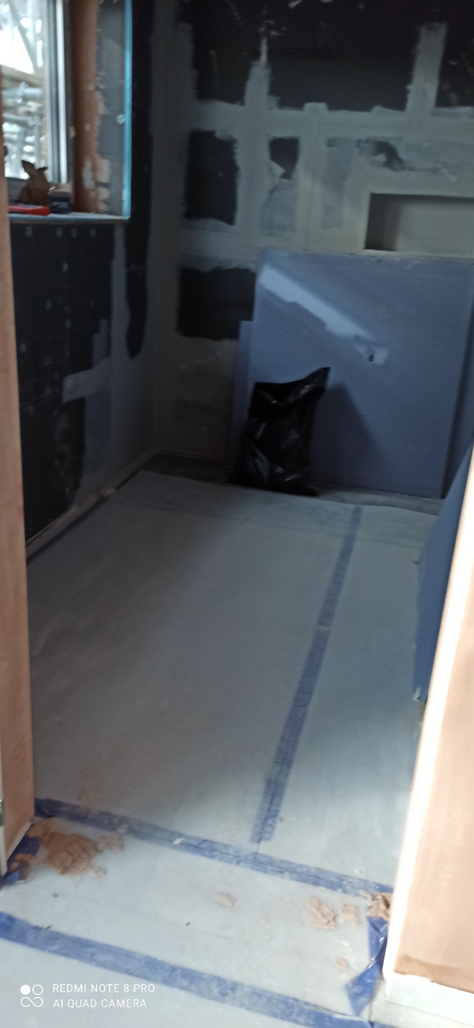 Przygotowanie do remontu łazienki: zabezpieczona podłoga folią, płyty karton gips oparta o ścianę, ściany z widocznymi śladami po gładzi.