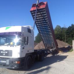 F.H.U. GACEK Szymon Gacek - Ciężarówka MAN z podniesioną czerwoną skrzynią ładunkową, wysypująca piasek na placu budowy w słoneczny dzień.