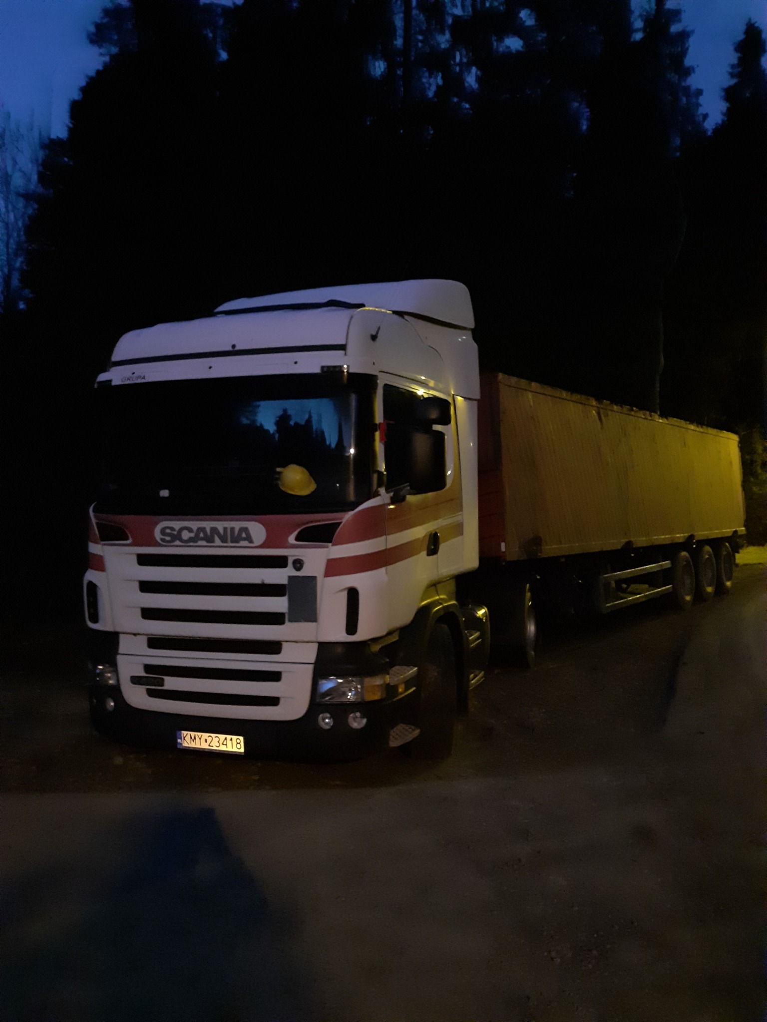 Ciężarówka Scania z naczepą na poboczu drogi w nocy, na desce rozdzielczej leży żółty kask.
