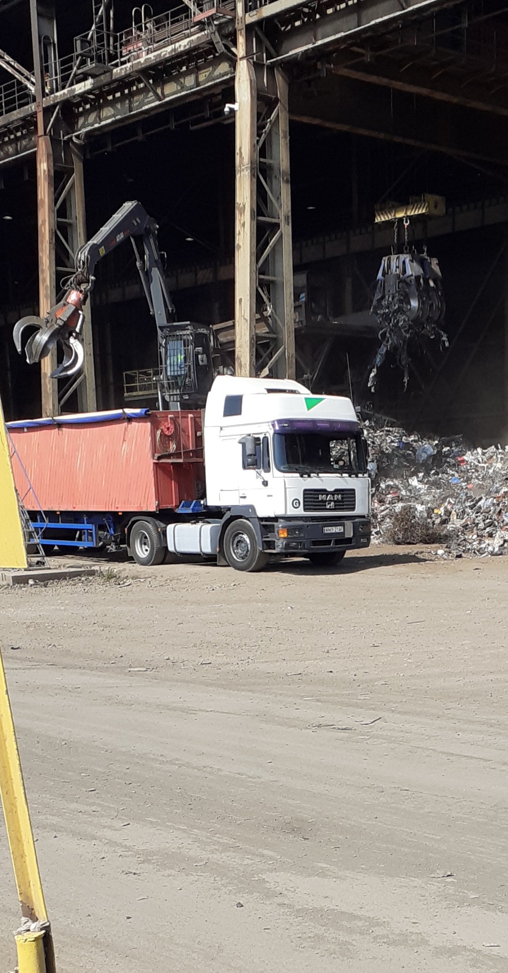 Ciężarówka MAN w Skomielnej Białej podnoszona przez dźwig na tle hali z odpadami metalowymi.