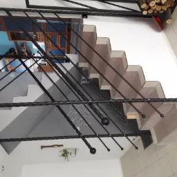 Wewnętrzne schody z kutą, czarną balustradą, widok z dołu, dekoracje ścienne w tle.