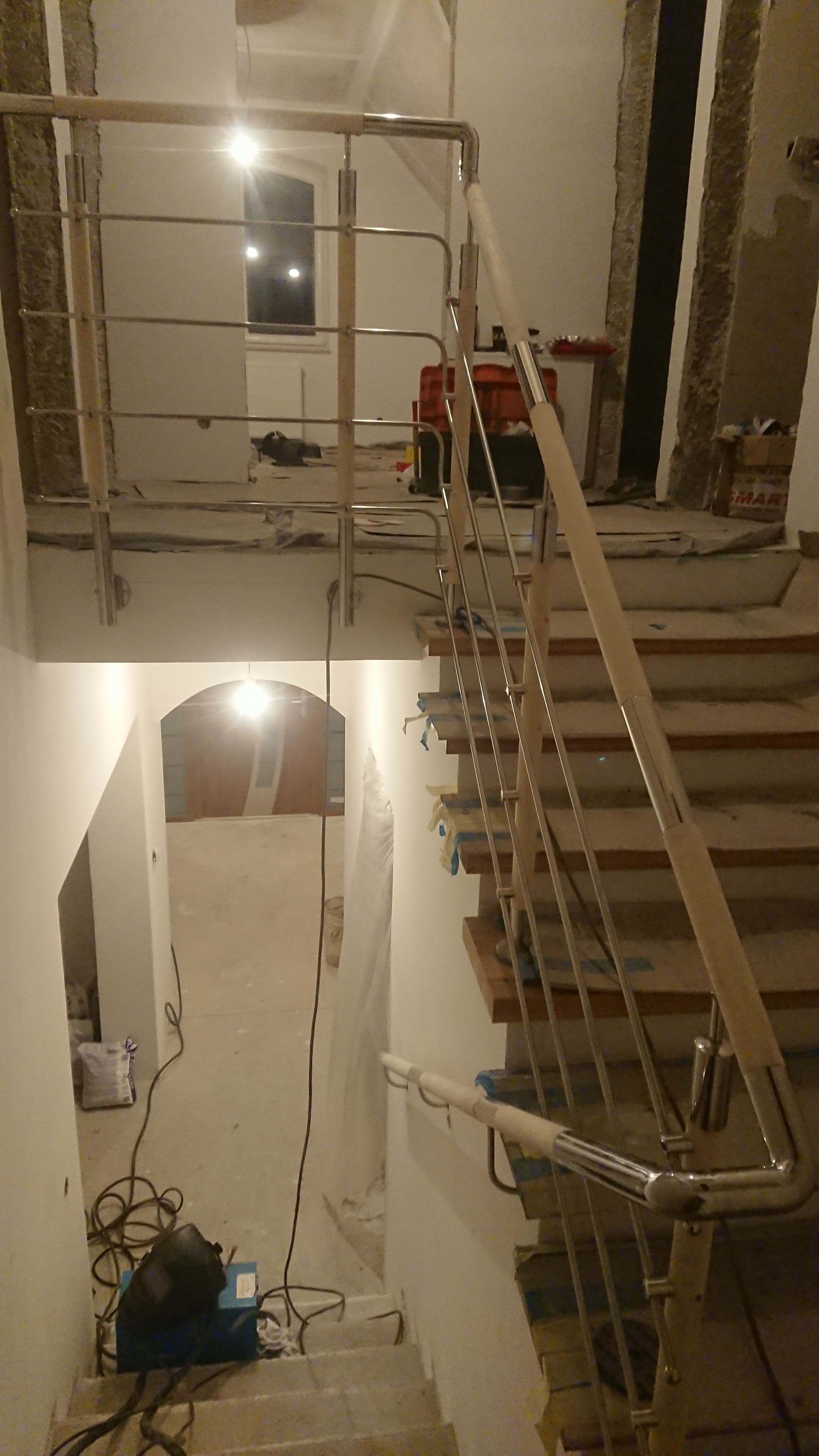 Montaż poręczy ze stali nierdzewnej na schodach wewnętrznych, widoczny sprzęt spawalniczy i materiały budowlane.