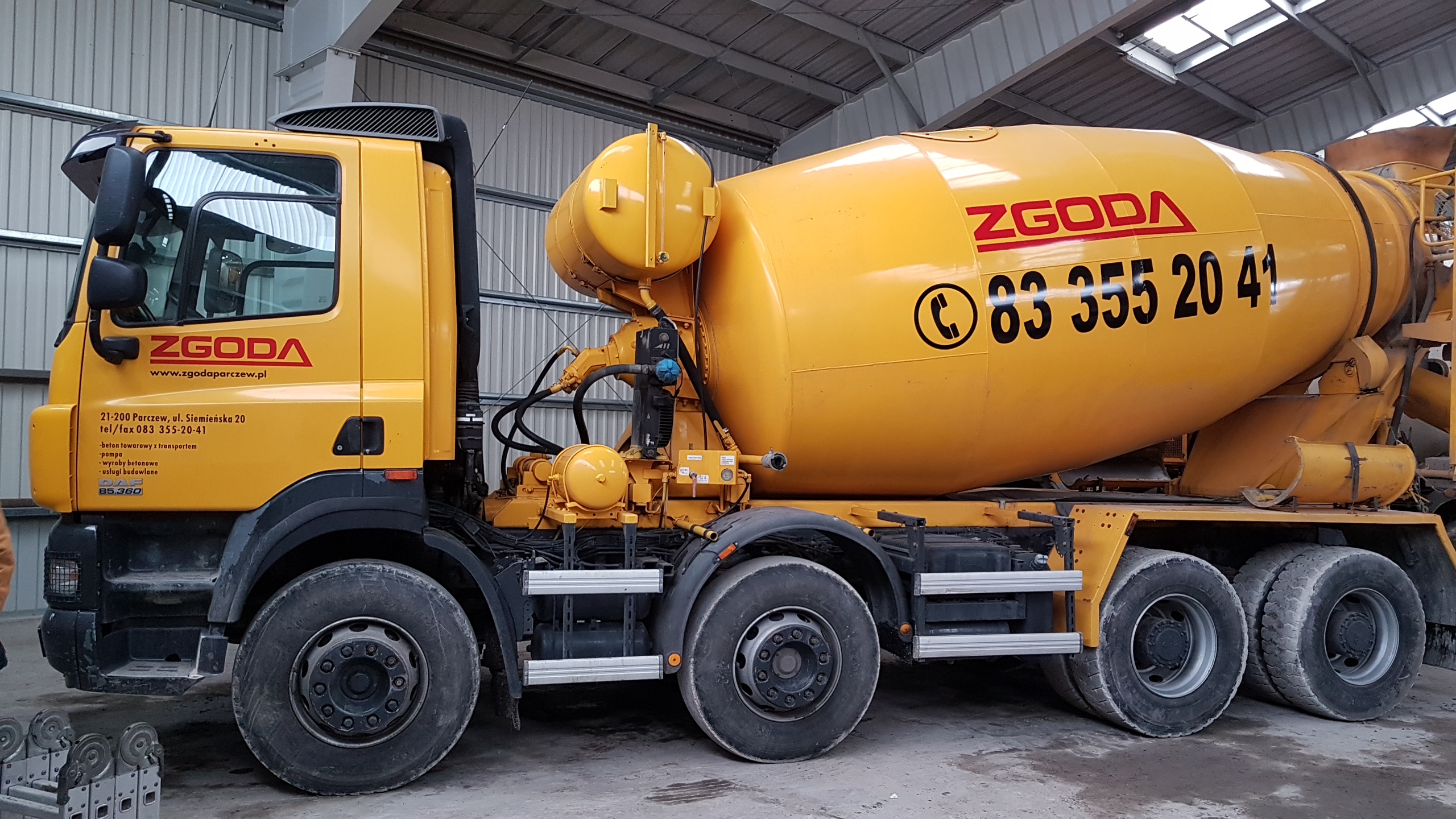 Żółta betonomieszarka firmy ZGODA z numerem telefonu, zaparkowana w hali.