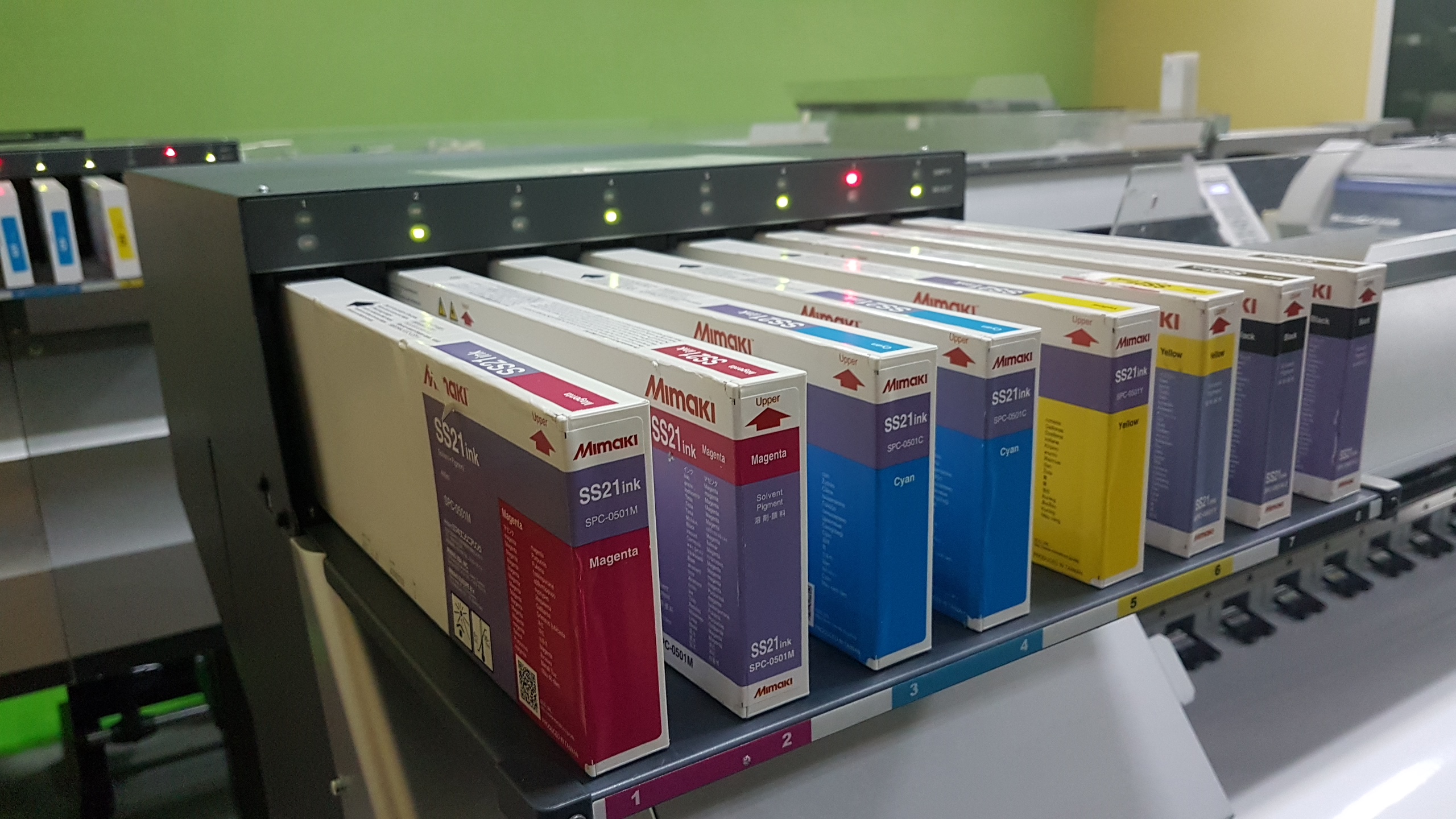 Rząd kolorowych pudełek z tuszem Mimaki SS21ink w zasobniku drukarki wielkoformatowej, widoczne kolory magenta, cyan, yellow i black.