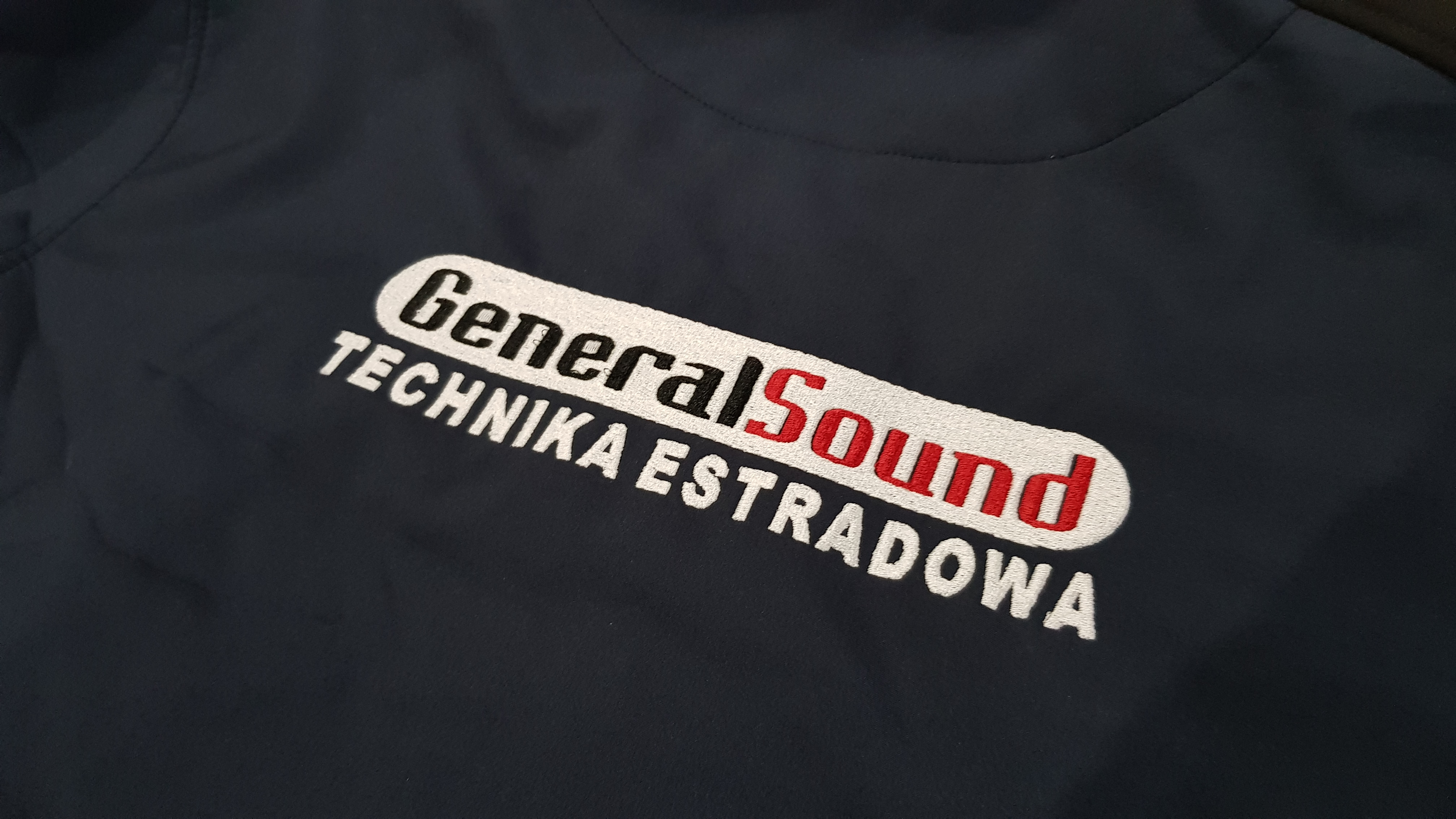 Granatowa kurtka z wyhaftowanym logo firmy GeneralSound Technika Estradowa, widoczne detale haftu.
