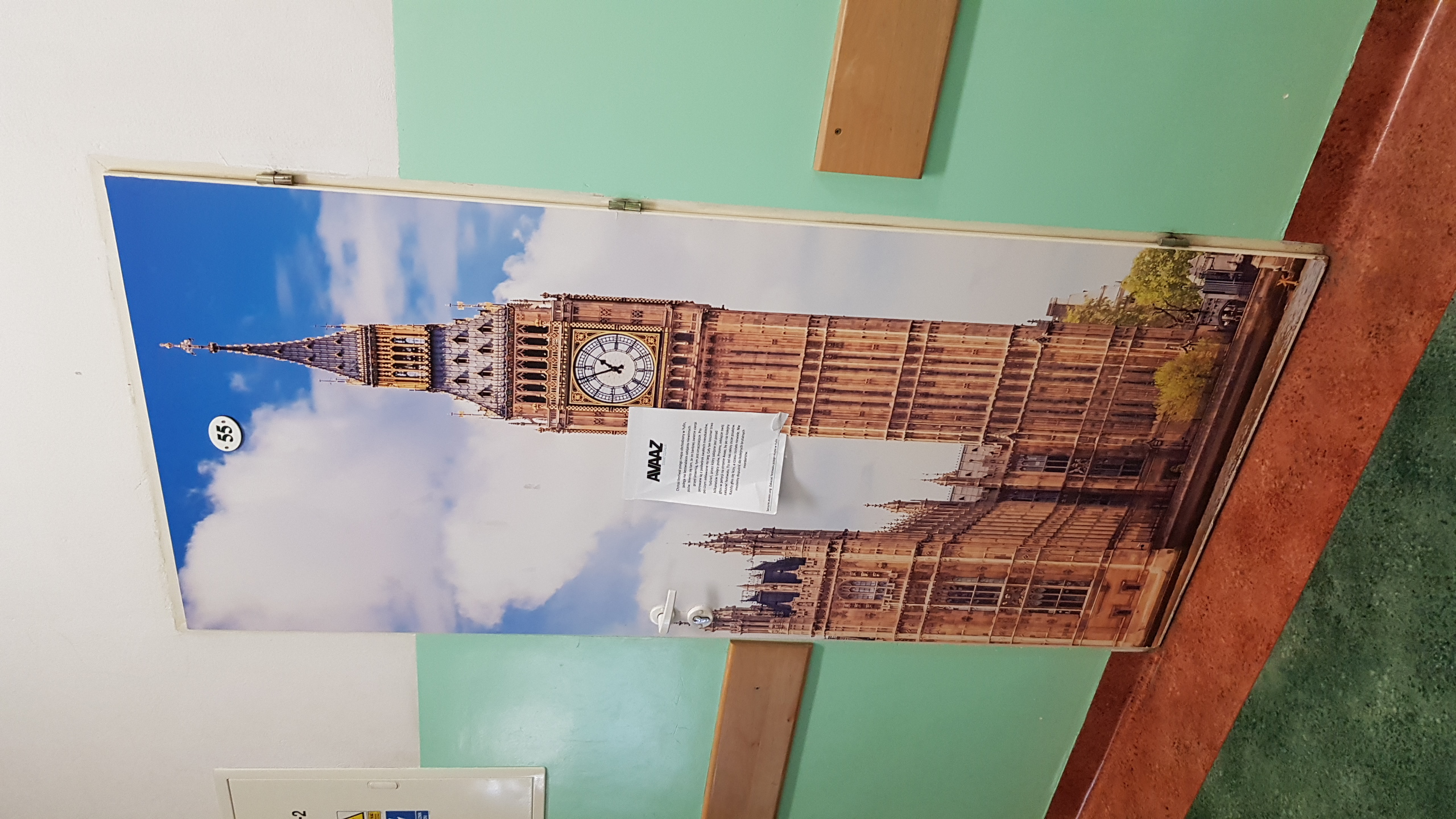 Druk wielkoformatowy na drzwiach przedstawiający Big Ben w Londynie, widoczny numer pokoju '55' i ulotka informacyjna AVAZ.
