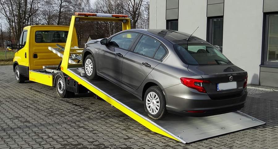 Żółta laweta z szarym samochodem osobowym na platformie, widok z tyłu, kostka brukowa