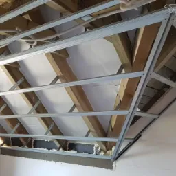 Konstrukcja metalowa poddasza z widoczną izolacją termiczną i drewnianymi elementami więźby dachowej, przygotowana do dalszych prac wykończeniowych.