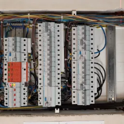 Rozdzielnia elektryczna z widocznymi bezpiecznikami, przewodami o różnych kolorach oraz elementami zabezpieczającymi, z laserowo wyznaczonym poziomem na ścianie.