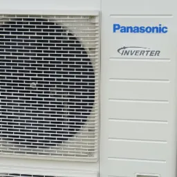 Biała zewnętrzna jednostka klimatyzacji Panasonic Inverter z kratką wentylacyjną.