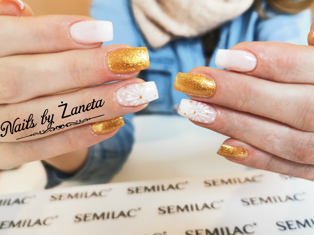 Dłonie prezentujące stylizację paznokci w Sosnowcu: jeden paznokieć biały, drugi złoty brokat, a trzeci z białym wzorem płatka śniegu i złotymi kropkami. Widoczne produkty Semilac.